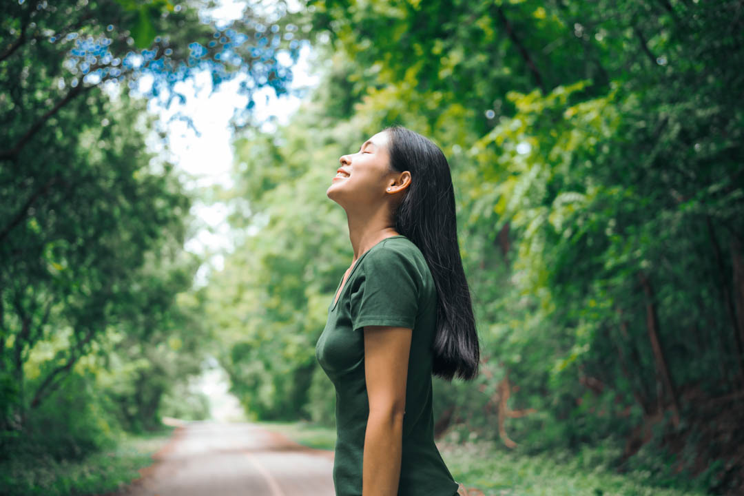 An Asian woman is standing happily in a green forest park, enjoying the fresh air and nature