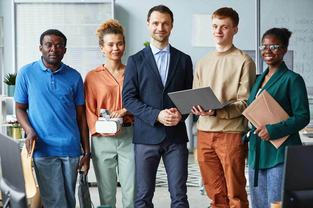 Portrait of group of programmers standing with gadgets and looking at camera during teamwork at office